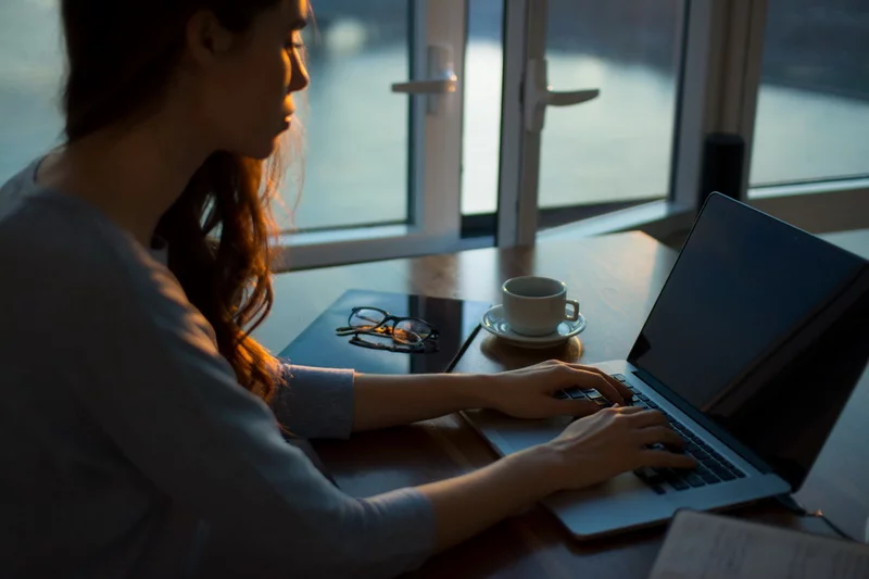 Devojka na poslu radi na laptopu i pije svezu kafu za dodatnu energiju.